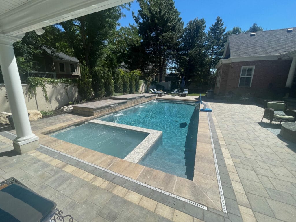 Utah custom pool with infinity hot tub, fire pit, and custom concrete paver patio