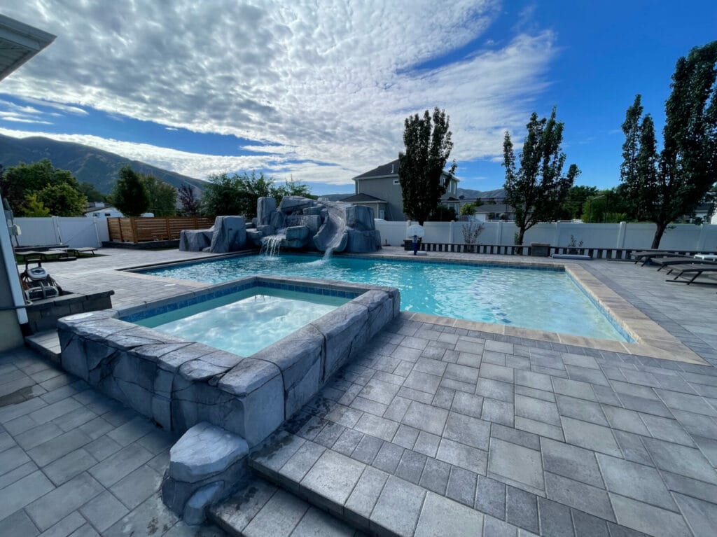 Custom swimming pool with natural rock waterfall design, slide, hot tub, and custom pool deck patio in Salt Lake City, Utah backyard - Stevenson Brothers Custom Pools - SBI Waterfalls
