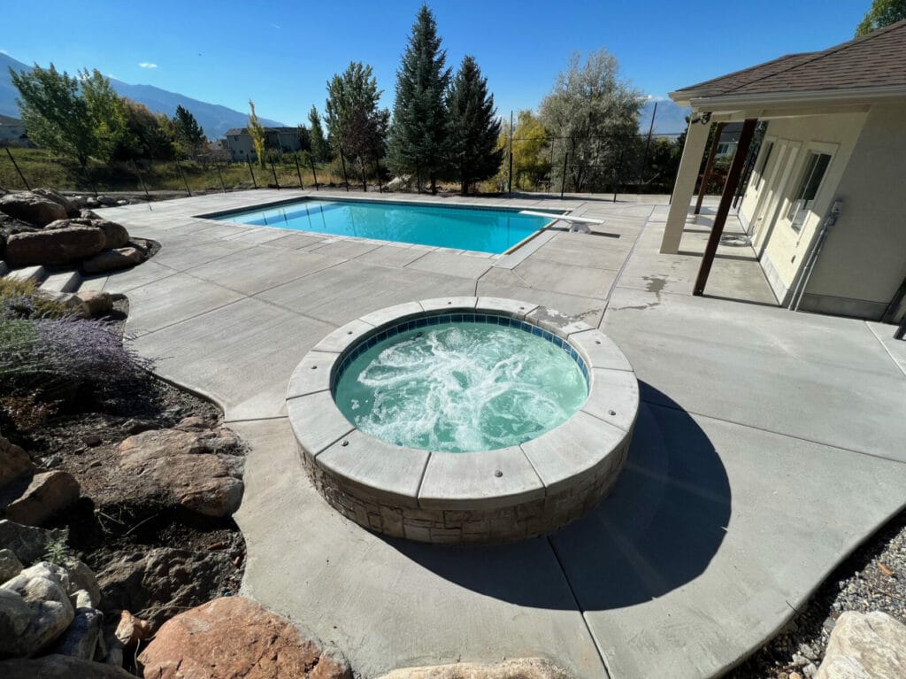 round hot tub & custom swimming pool with diving board and new concrete patio and landscaping in Utah