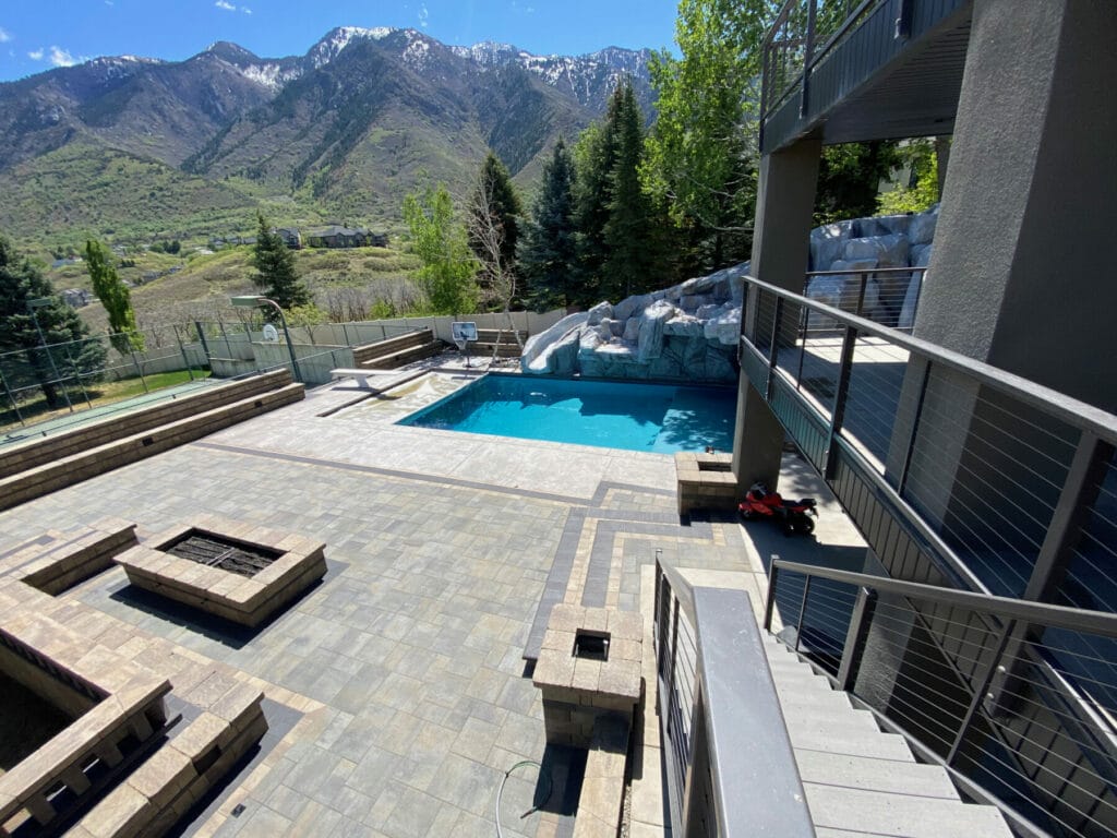 Salt Lake City custom pool and modern stone patio with natural rock pool slide, waterfalls, fire pits, and a basketball court designed and built by Stevenson Brothers Custom Pools