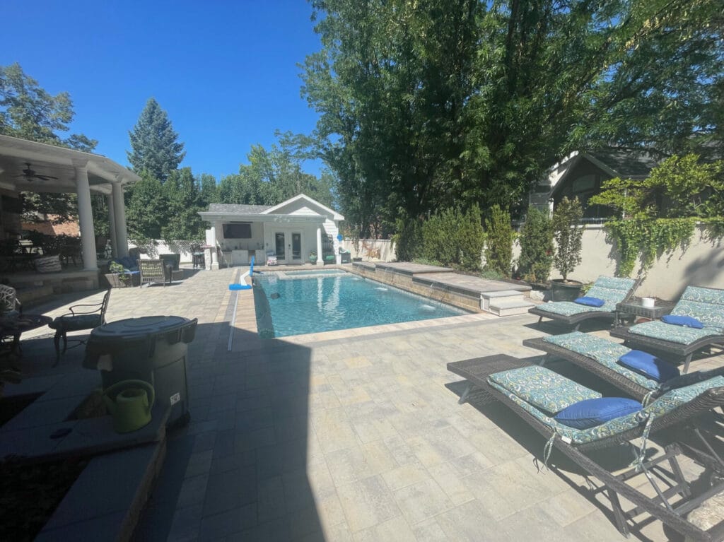 Utah custom pool with infinity hot tub and waterfalls features a modern hardscaping design style